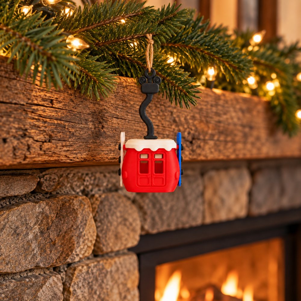 Red gondola ornament hanging from a fir garland on a wooden mantel with warm lights and a stone fireplace